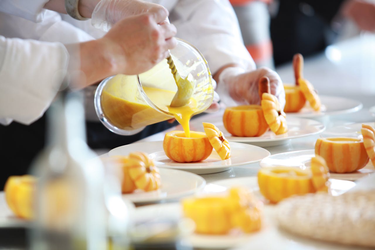 heros-img Chef performing culinary artistry by pouring vibrant pumpkin soup in decorative pumpkins.